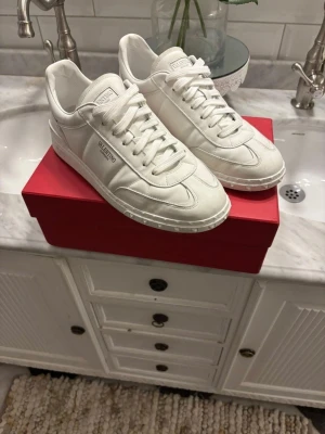 Valentino Garavani upvillage - Säljer ett par stilrena vita sneakers från Valentino Garavani. Skorna har en låg profil, rund tå och platt sula med coola nitar längs kanten. Tillverkade i skinn med snygga sömmar och klassisk snörning. Perfekta för dig som gillar exklusiva och cleana sneakers. Storlek 43 passar +-1, mycket bra skick, bara att skriva för frågor 