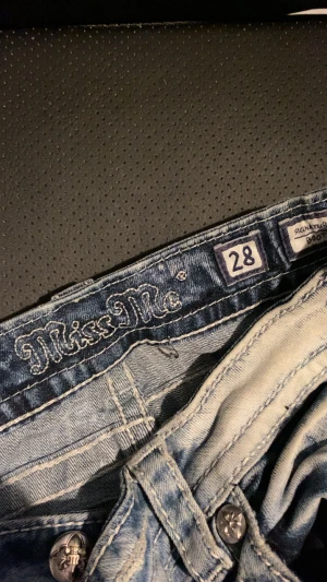 Miss Me bootcut jeans med broderi - Säljer ett par Miss Me jeans i storlek 28 med snyggt broderade bakfickor och dekorativa knappar. Jeansen är ljusblå med tvättad look och har bootcut-snitt. Materialet är klassisk jeans i bomull och passformen är loose med låg midja. Finns lite färg fläckar på dem därefter priset!