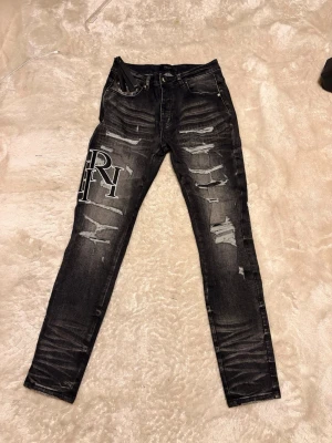 Amiri jeans  - Säljer ett par svarta skinny jeans från AMIRI med slitna detaljer och stora vita tryck på benen. Jeansen har klassisk femficksdesign, dragkedja och knapp i midjan. Materialet är jeans med stretch och de har en riktigt cool streetstil.