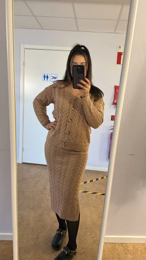 Beige stickad kofta med knappar - Säljer en beige stickad kofta med snyggt flätmönster och stora knappar framtill. Koftan har v-ringad hals och långa ärmar, perfekt att matcha med kjol eller jeans. Den är loose fit och riktigt mysig för kyliga dagar.