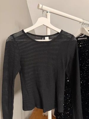 Svart ribbad långärmad topp XS - Säljer en svart långärmad topp från Divided i storlek XS. Toppen är ribbad med genomskinliga vertikala ränder och är aldrig andvänd🤍