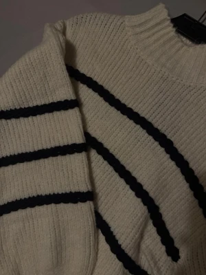 Randig stickad tröja med polokrage - Säljer en mysig stickad tröja i offwhite med svarta, grova ränder. Tröjan har polokrage och är långärmad med loose passform. Perfekt för dig som gillar klassisk stil med en twist. Materialet är tjockt och ribbstickat, vilket gör den extra skön under kyliga dagar.