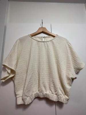 luftig tröja med resårband - crème-färgad, blusaktig tröja i luftigt och texturerat material! tröjan har en knapp vid nacken och ett resårband längst ner. okänt märke