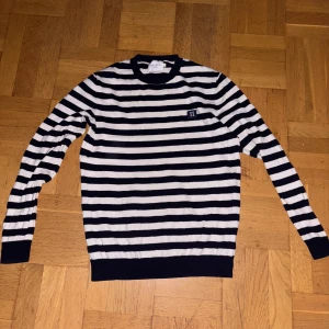 Randig stickad tröja från Les Deux - Snygg stickad tröja från Les Deux med marinblå och vita horisontella ränder. Rund halsringning och långärmad modell, med liten logotyp på bröstet. Perfekt för dig som gillar klassisk och stilren design.