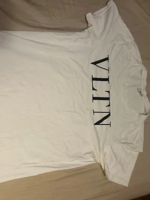 Vit VLTN t-shirt från Valentino - Säljer en clean vit t-shirt från Valentino med stor svart VLTN-logga över bröstet. Klassisk rund hals och korta ärmar. Perfekt basic med lyxig touch, tillverkad i mjuk bomull som känns skön mot huden.