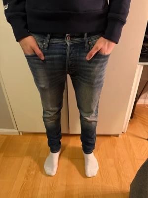 Blå skinny jeans från Jack & Jones - Säljer ett par blå skinny jeans från Jack & Jones med snygga slitningar och klassisk femficksdesign. Jeansen har normal midja och är tillverkade i stretchig denim för en bekväm passform. Perfekta för dig som gillar en smal siluett och stilren look.