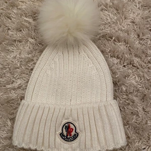 Vit stickad mössa från Moncler - vit stickad mössa från Moncler med en fluffig pälsboll. Se alla bilder finns smink fläckar i mössan som inte syns inte testat tvättat bort dessa.