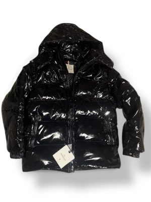 Moncler Jacka - Säljer en svart, glansig pufferjacka från Moncler. Perfekt för dig som vill ha en snygg och varm jacka till vintern. Jackan har en autentisk NFC tag samt en autentisk QR kod. Samt påsen finns kvar och det sitter fortfarande tags och skyddsplast på dragkedjan för fickor. Storleken är Medium