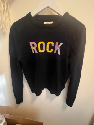 Svart stickad tröja Zadig & Voltaire - Cool svart stickad tröja från Zadig & Voltaire med färgglad 'ROCK'-text framtill. Tröjan har rund hals, lång ärm och ribbade muddar. Perfekt för dig som gillar statement-plagg och vill ha en unik look.