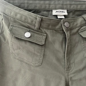 Gröna byxor med fickdetaljer från Monki - Snygga gröna byxor från Monki med raka ben och coola fickor framtill med lock och silverfärgade knappar. Byxorna har bälteshällor och stängs med knapp och dragkedja. Perfekta för en chill och trendig look.