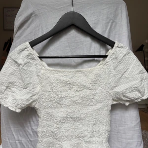 Vit topp med puffärm - Supersöt vit topp med puffärmar och smockad struktur i storlek 158/164 men är som en Xs, ifrån Kappahl! Toppen är i ett texturerat tyg som ger en cool och fräsch vibe. Inga defekter!!! Kontakta mig om du har några funderingar!!❤️