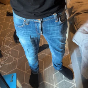 nudie slim fit jeans - Säljer ett par klassiska blå jeans från nudie med snyggt slitna detaljer och raka ben. Jeansen har fem fickor, orange sömmar och läderpatch bak i midjan. Perfekta för dig som gillar en tidlös och avslappnad look.