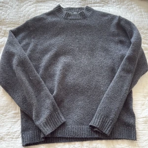 Mörkgrå stickad tröja från Uniqlo - Säljer en stilren mörkgrå stickad tröja från Uniqlo i storlek M. Tröjan har rund hals, ribbade muddar vid ärmslut och nederkant samt långärmad passform. Perfekt för dig som gillar enkel och clean look med mjukt material.