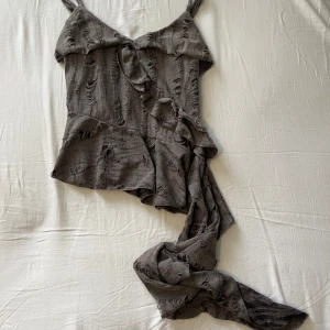 Grå omlott topp med volang och snörning - Säljer en super snygg topp som jag aldrig har använt så den är helt ny! Den är så fin och cool💕
