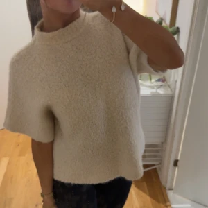 Beige stickad kortärmad tröja - Supermjuk och fluffig beige stickad tröja med boxig passform och korta ärmar. Perfekt till både jeans och kjol, med hög halsringning och enkel design. Ger en chill och trendig vibe till din outfit.