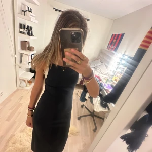 Svart långklänning med smala axelband - En stilren svart långklänning med smala axelband och rak passform. Klänningen har en enkel design utan mönster och ärmlös modell, perfekt för dig som gillar minimalistisk stil. Materialet känns mjukt och följsamt mot kroppen.