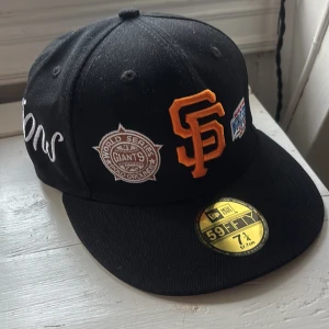 Svart San Francisco Giants keps New Era - Säljer en svart 59FIFTY keps från New Era med San Francisco Giants brodyr i orange och flera broderade patches. Kepsen har platt skärm, broderade detaljer och MLB-logga bak. Perfekt för dig som gillar baseball och streetwear.
