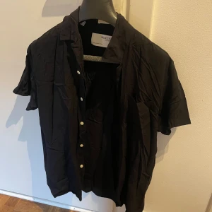 Svart kortärmad skjorta Selected Homme - Svart skjorta från Selected Homme med korta ärmar och klassisk krage. Skjortan har vita knappar framtill och en bröstficka. Perfekt för en stilren och enkel look.
