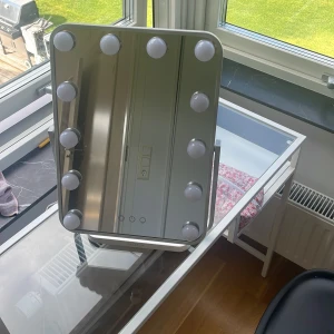 NOOA Hollywood sminkspegel med lampor - Snygg Hollywood-inspirerad sminkspegel från NOOA, modell Glow. Spegeln har 12 runda LED-lampor runt kanten och touchknappar för att justera ljusstyrka och färgtemperatur. Perfekt för att få till sminket med riktigt bra ljus. Spegeln är rektangulär och har vit ram.