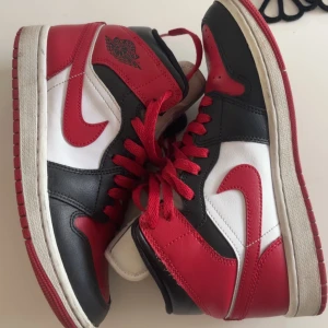 Nike Air Jordan 1 mid röd/svart/vit - Säljer ett par Nike Air Jordan 1 mid med klassisk färgkombination i rött, svart och vitt. Skorna har röda snören, svart och röd läderdetaljer samt vit bas. Äkta jordans!!! Storlek 37,5 