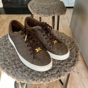 Bruna Michael Kors sneakers - Snygga bruna sneakers från Michael Kors med klassiskt logomönster och vita sulor i väldigt bra skick.