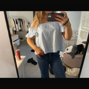 Ljusblå offshoulder blus - Superfin ljusblå blus med offshoulder och korta volangärmar. Tunt bomullstyg med diskreta ränder och avslappnad, croppad passform. Perfekt för varma dagar och ger en fräsch vibe till din outfit.