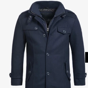 Mörkblå rock från Indigo med knappar - Snygg mörkblå rock från Indigo med klassisk krage, flera fickor och knappar framtill. Jackan har långa ärmar med knappdetaljer och är fodrad för extra värme. Perfekt för dig som vill ha en stilren och tidlös look under kallare dagar. Storlek XL sitter lagom i storleken, originalpris 1849kr, använd några enstaka gånger, säljer för att den va lite för stor för mig, tveka inte på att höra av er vid frågor