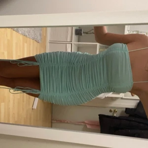 Mintgrön tight kortklänning med snörning - Supersnygg mintgrön kortklänning med smala axelband och rynkade detaljer längs hela klänningen. Tight passform och snörning i sidorna för extra effekt. Dragkedja bak för enkel påklädning. Perfekt för dig som vill sticka ut med en fräsch färg!