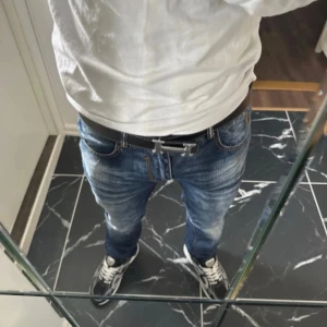 Svart skärp med H-spänne - Snyggt svart skärp från  med klassiskt H-spänne i silverfärg. Bältet är gjort i skinn och har vita kontrastsömmar längs kanterna. Perfekt accessoar för att lyfta din outfit med en exklusiv touch.