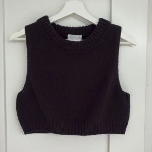 Svart stickad väst från & Other Stories - Svart stickad väst från & Other Stories Los Angeles Atelier. Modellen är croppad med bred ribbad kant vid halsringning och nederkant. Perfekt att styla över en skjorta eller t-shirt för en trendig lager-på-lager-look.