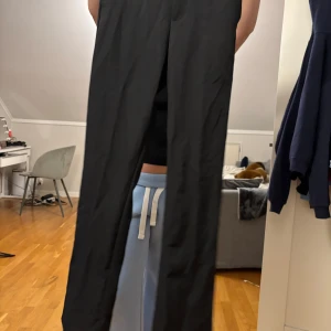 Svarta kostymbyxor från Bik Bok - Svarta kostymbyxor från Bik Bok i storlek 34. Byxorna har en rak och klassisk passform med midja och är tillverkade i ett mjukt material med inslag av polyester och viskos. Perfekta för en clean och stilren look.