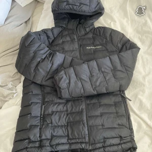 Svart pufferjacka Peak Performance - Säljer en svart pufferjacka från Peak Performance med huva och dragkedja framtill. Jackan har quiltad design och två fickor med dragkedja. Perfekt för hösten, frågor? Bara att skriva. Storlek 160, ny kostar 1800kr