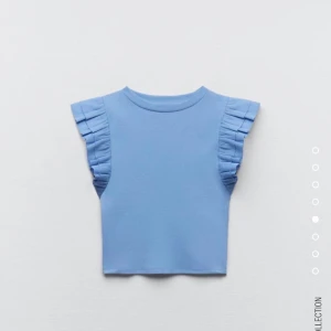 Ljusblå volangtopp med ärmlös design - Supersöt ljusblå topp med volangdetaljer vid axlarna och ärmlös design. Croppad passform som ger en trendig look. 