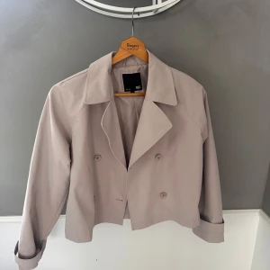 Beige croppad trenchcoat från 157 - Säljer en beige croppad trenchcoat från 157 med klassisk krage och dubbelknäppning.  #lager157 #trenchcoat 