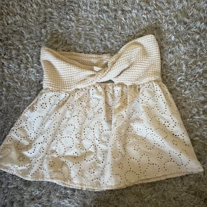 Beige bandeau tubtopp med broderade blommor - Supersöt beige bandeau tubtopp med virkad överdel och broderade blommor på den vida nederdelen. Toppen är axelbandslös och har en lätt volangkant. Perfekt för varma dagar och ger en romantisk vibe.