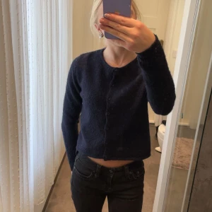 Mörkblå kofta från Gina Tricot - Mysig mörkblå kofta från Gina Tricot i stickad kvalitet. Modellen är croppad med rund halsringning och knappar framtill. Perfekt att slänga över en topp för en chill look. Långärmad och enkel att matcha med jeans eller kjol. Sparsamt använd, i mycket fint skick!