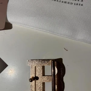 Burberry bälte med guldspänne - Säljer ett Burberry bälte med klassiskt rutigt mönster i beige, svart och rött på ena sidan och svart präglat skinn med Burberry-logga på andra sidan. Stort B-format spänne i guld. Kommer med originalpåse, box och kvitto.