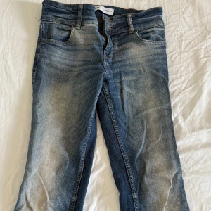 Blå bootcut låg/mellanmidjade jeans - Säljer ett par klassiska blå jeans med snygga slitningar och tvättade detaljer. Jeansen köpta från bershak i bra skick, med två knappar. Köpta för 400kr