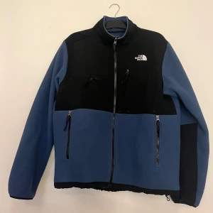 Blå och svart fleecejacka The North Face - Säljer en blå och svart fleecejacka från The North Face med dragkedja framtill och flera fickor med dragkedja. 