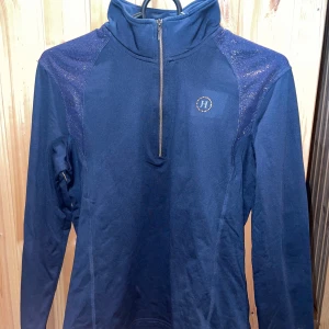 Marinblå half zip tröja JH Collection - Snygg marinblå långärmad tröja från JH Collection med glittriga detaljer på axlarna och praktisk half zip framtill. Hög krage och sportig look, perfekt för dig som gillar stilren design och funktion. Säljes då jag slutat rida