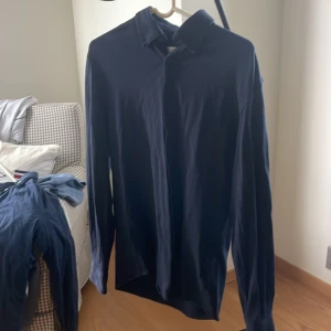 Mörkblå skjorta från Selected Homme - Snygg mörkblå skjorta från Selected Homme i slim fit-modell. Skjortan har klassisk krage, långa ärmar och knäppning framtill. Perfekt för dig som gillar stilrena och enkla plagg med en modern passform.