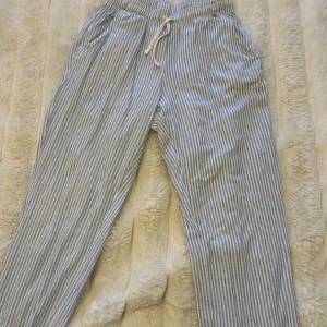 Randiga pyjamasbyxor - Säljer ett par ljusblå och vita randiga pyjamasbyxor från s.Oliver. Byxorna har dragsko i midjan, raka ben och sidfickor. Perfekta för chill dagar eller när du vill ha en avslappnad look.