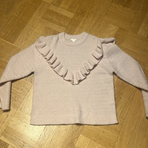 Ljusrosa stickad tröja med volang Gina Tricot - Superfin ljusrosa stickad tröja från Gina Tricot i storlek 158/164 men stor i storleken. Tröjan har en snygg volangdetalj som går diagonalt över framsidan och axeln. Mjuk och mysig, perfekt för kyliga dagar. Långärmad och med diskret mönster i stickningen.