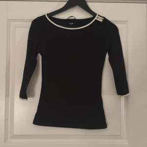 Svart topp med guld  knappar - Super snygg svart trekvartsärmad tröja med vita detaljer och guldknappar vid kragen. Använd några gånger men inga täcken på användning. 