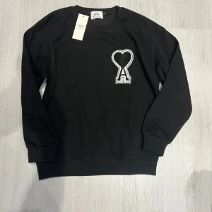 Svart sweatshirt från Ami Paris - Svart sweatshirt från Ami Paris med ikonisk broderad logga i form av ett hjärta och bokstaven A på bröstet. Tröjan har rund hals, långa ärmar och ribbade muddar. Tillverkad i mjuk bomull för en skön och avslappnad vibe. ‼️Pris är ännu inte hugget i sten så kom med förslag!‼️