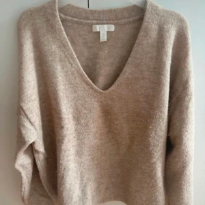 Beige stickad v-ringad tröja H&M - Mysig beige stickad tröja från H&M med djup v-ringning och lång ärm. Tröjan har en loose passform och är perfekt för lager-på-lager. Ribbstickade muddar vid ärmslut och nederkant ger en snygg detalj. Superenkel att styla till jeans eller kjol. Tröjan är lite noppig