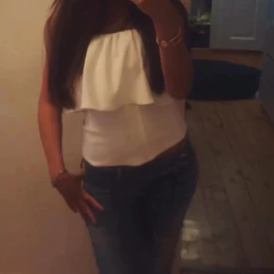 Vit bandeau tubtopp med volang - Säljer en fräsch vit bandeau tubtopp med bred volang upptill. Toppen är axelbandslös och har en snygg croppad passform som sitter tight mot kroppen. Perfekt för dig som vill ha en clean och stilren look .