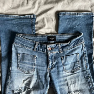 Lågmidjade jeans  - Lågmidjade bootcut jeans med hål ifrån Vero Moda. Storlek 29/34. Nypris: 699 kr. En tyglapp är insydd på insidan av jeansen för ökad hållbarhet men det är inget som syns!