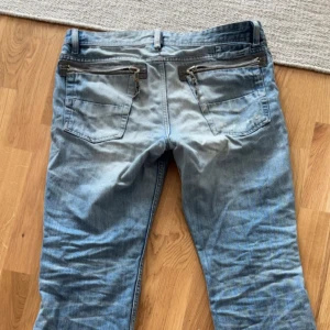 Blå jeans från Diesel - Säljer ett par ljusblå jeans från Diesel med slitningar på låren och snygga dragkedjor på bakfickorna. Klassisk femficksmodell med logotyp på myntfickan. Jeansen är i denim och har en avslappnad vibe.