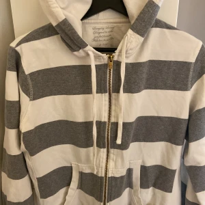 Zip-up hoodie  -  Vit zip-up hoodie från Ellos med gråa, breda ränder ✨ Huvan har snörning, framficka och dragkedja, perfekt för mysiga dagar eller till vardags🖤Kan stylas med kjol, jeans eller t-shirt! Storlek X-Large, men sitter snyggt även på XS/S för en trendig oversized look!
